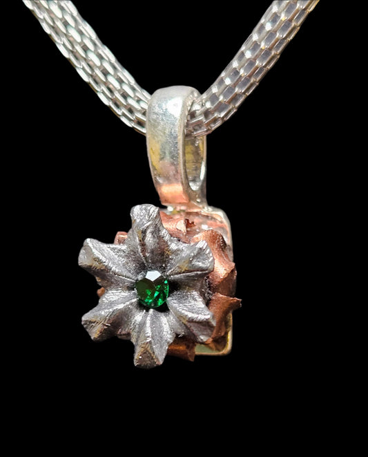 Emerald green colored crystal in the center of a hollowpoint bullet pendant on a silver colored mesh chain necklace. 